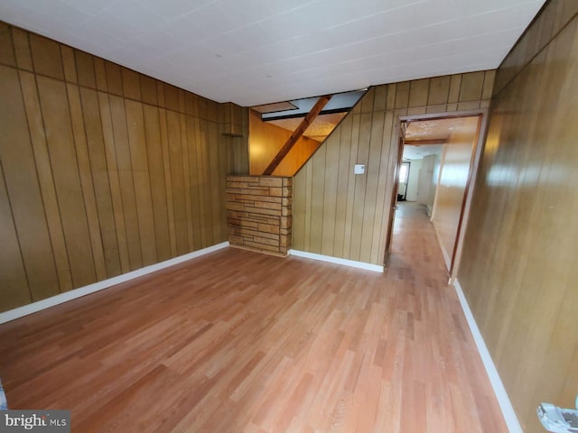 empty room featuring light wood-type flooring, wooden walls, and baseboards