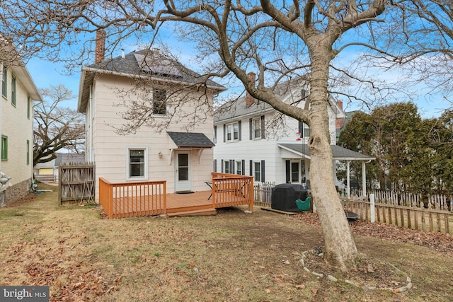 back of property with a chimney, fence, a lawn, and a wooden deck