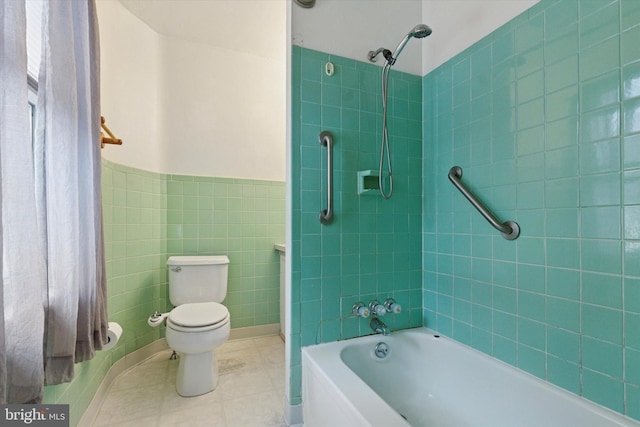 bathroom with tile walls, shower / bathtub combination, toilet, wainscoting, and tile patterned flooring