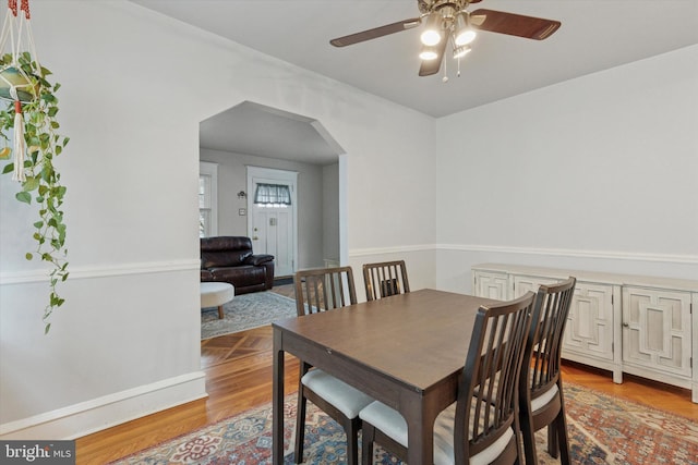 dining room featuring a ceiling fan, arched walkways, and light wood finished floors