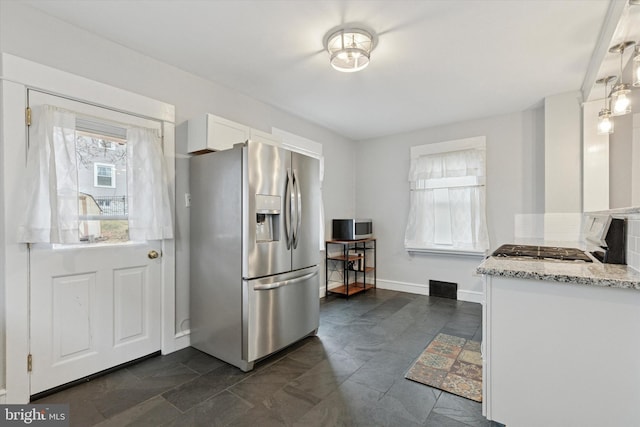 kitchen featuring light stone counters, white cabinetry, stainless steel refrigerator with ice dispenser, and baseboards