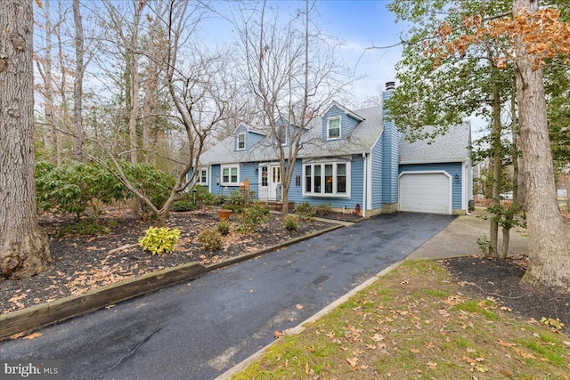 new england style home featuring driveway, an attached garage, and a chimney