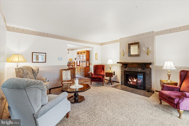 carpeted living room featuring a fireplace with flush hearth, a wainscoted wall, and wallpapered walls