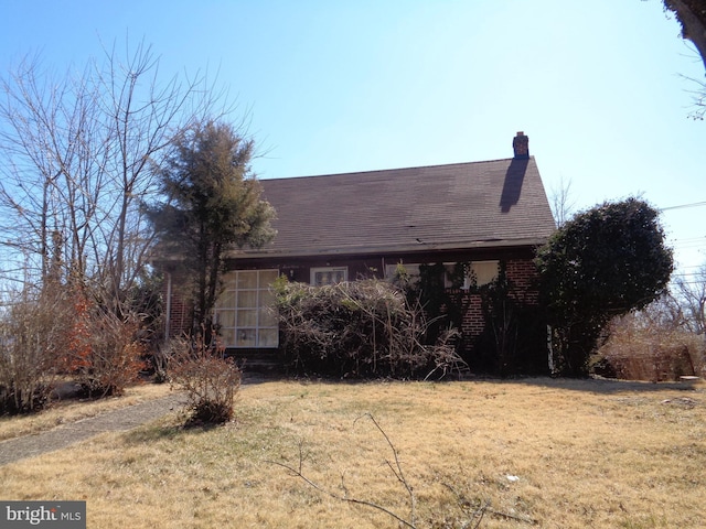 view of property exterior with brick siding, a chimney, and a yard