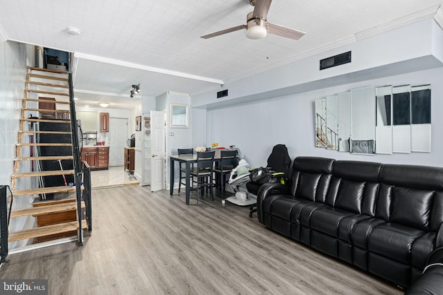 living room featuring visible vents, crown molding, light wood-style flooring, and stairs