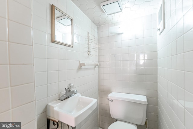 bathroom with toilet, tile walls, and a sink