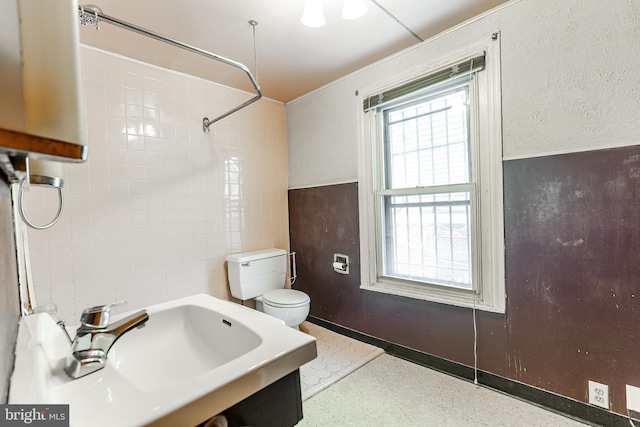 full bath featuring toilet, a sink, and tile walls