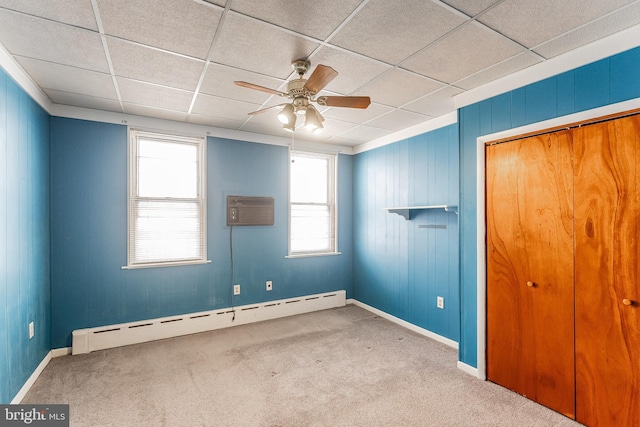 carpeted empty room with ceiling fan, a baseboard radiator, a paneled ceiling, baseboards, and a wall mounted air conditioner