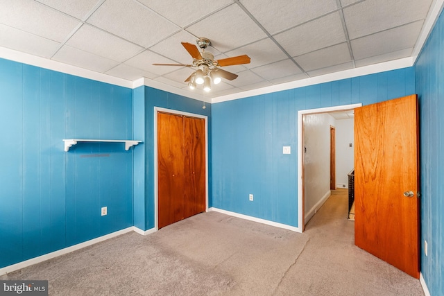 unfurnished bedroom with carpet floors, a paneled ceiling, a closet, and a ceiling fan