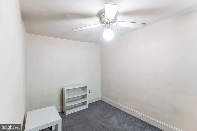 unfurnished room with a ceiling fan, dark carpet, and baseboards