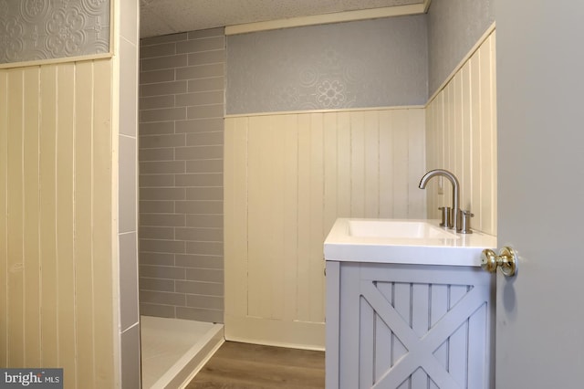 full bathroom featuring a wainscoted wall, tiled shower, wood finished floors, and vanity