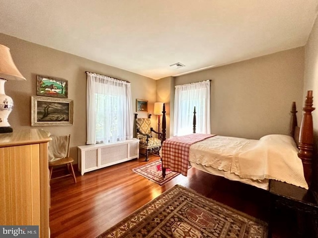 bedroom with wood finished floors, visible vents, and radiator