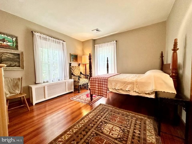 bedroom with radiator heating unit, wood finished floors, and visible vents