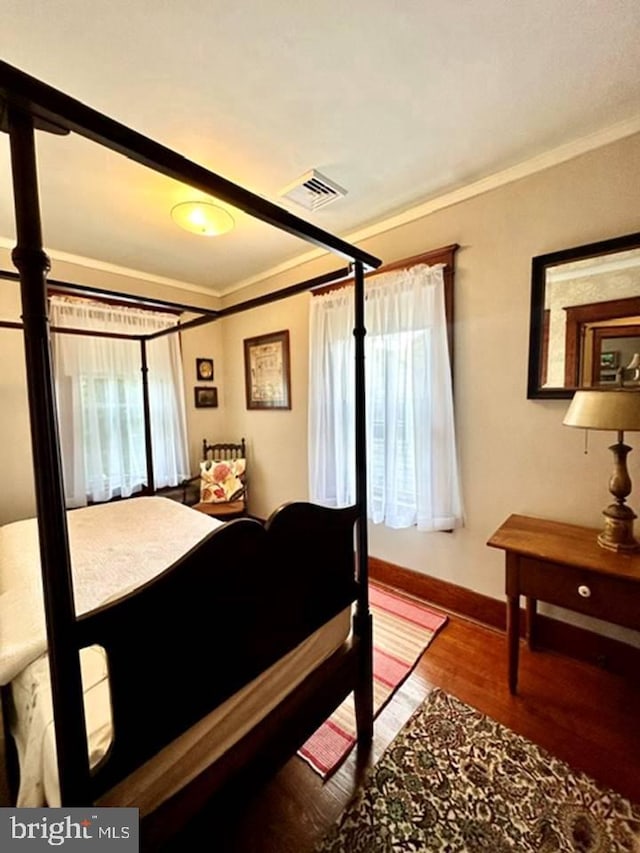 bedroom with ornamental molding, wood finished floors, visible vents, and baseboards