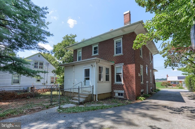 view of front of house with entry steps, brick siding, fence, and a chimney