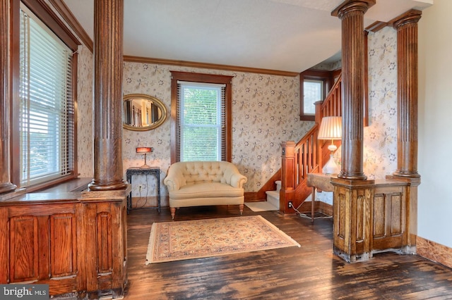 sitting room featuring stairs, wallpapered walls, dark wood finished floors, decorative columns, and crown molding