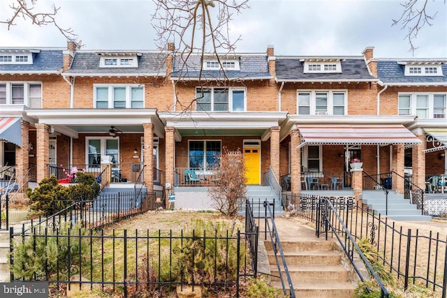 view of property featuring covered porch, a fenced front yard, mansard roof, and brick siding