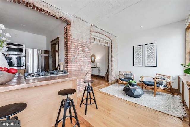 kitchen with brick wall, appliances with stainless steel finishes, a breakfast bar, and wood finished floors