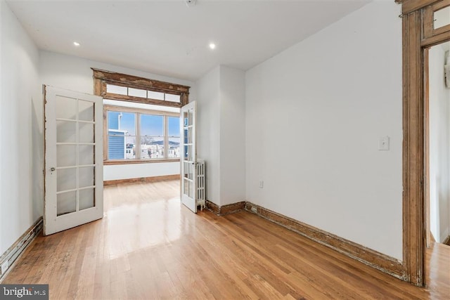 unfurnished room featuring french doors, a baseboard radiator, recessed lighting, light wood-type flooring, and baseboards