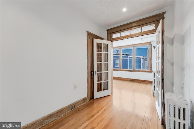 unfurnished room with french doors, baseboards, light wood-style flooring, and radiator heating unit