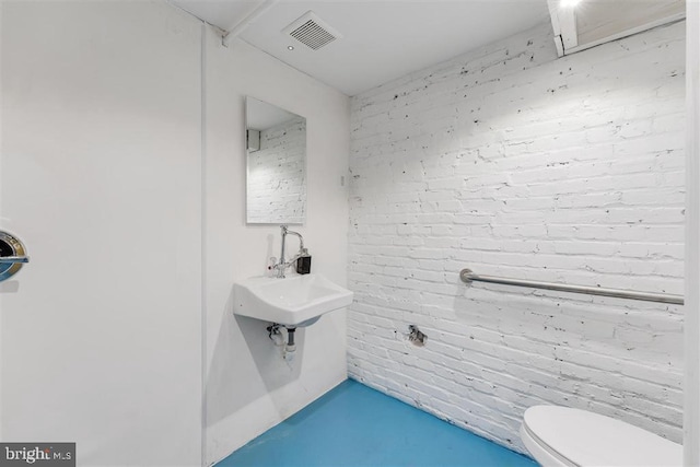 half bath featuring toilet, brick wall, visible vents, and a sink