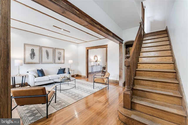 living area featuring arched walkways, baseboards, stairway, and light wood finished floors