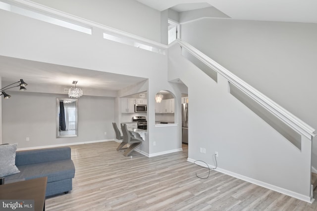 living room featuring light wood-type flooring, a high ceiling, arched walkways, and baseboards