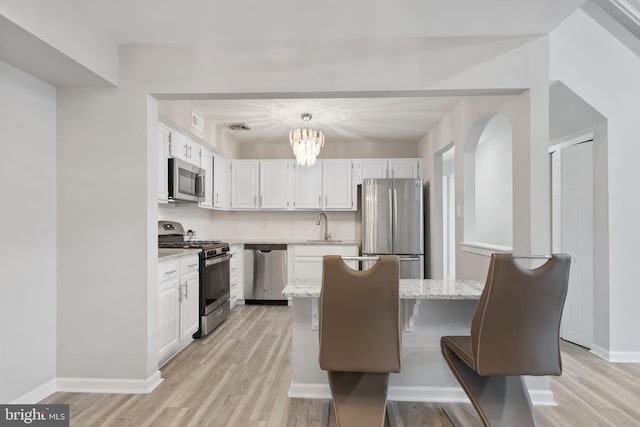 kitchen featuring appliances with stainless steel finishes, light wood-type flooring, white cabinets, and light stone counters