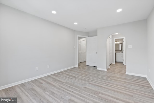 unfurnished bedroom featuring arched walkways, recessed lighting, light wood-type flooring, and baseboards