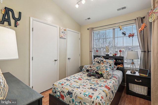 bedroom with a closet, visible vents, vaulted ceiling, and wood finished floors