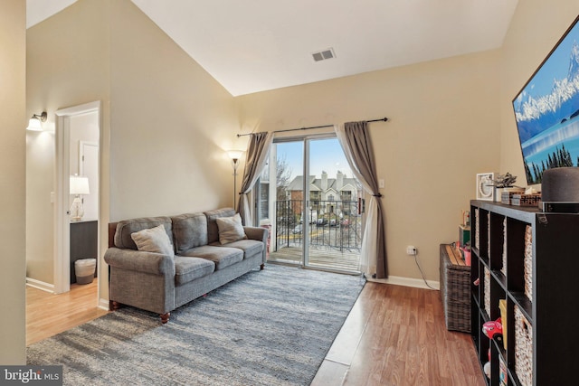 living area with high vaulted ceiling, baseboards, visible vents, and wood finished floors