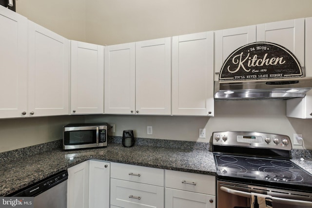 kitchen featuring appliances with stainless steel finishes, dark stone countertops, white cabinetry, and wall chimney exhaust hood