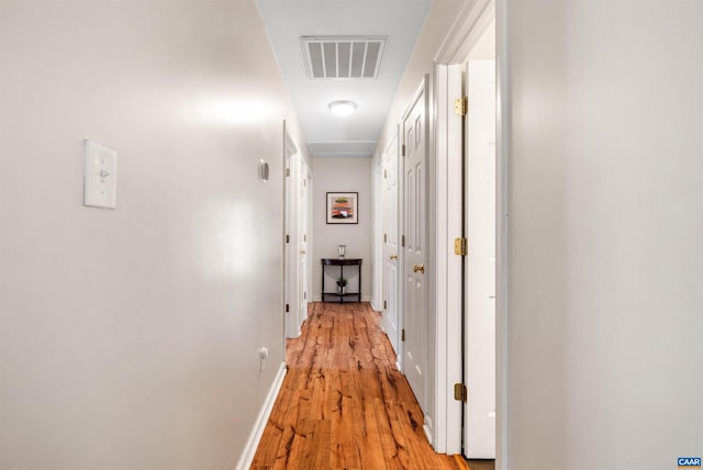 hallway featuring light wood-style floors, baseboards, and visible vents