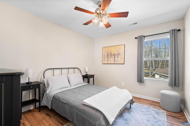 bedroom featuring a ceiling fan, visible vents, baseboards, and wood finished floors