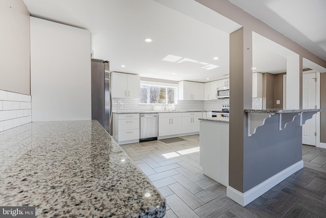 kitchen featuring a breakfast bar area, white cabinets, appliances with stainless steel finishes, decorative backsplash, and light stone countertops