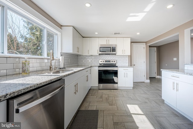 kitchen with white cabinets, decorative backsplash, stainless steel appliances, and a sink