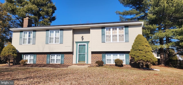 bi-level home with a front lawn, a chimney, and brick siding