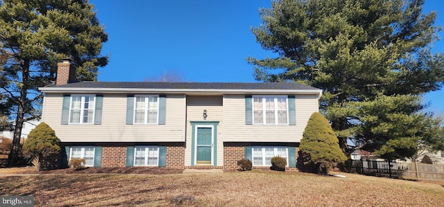 raised ranch featuring brick siding, a chimney, a front lawn, and fence