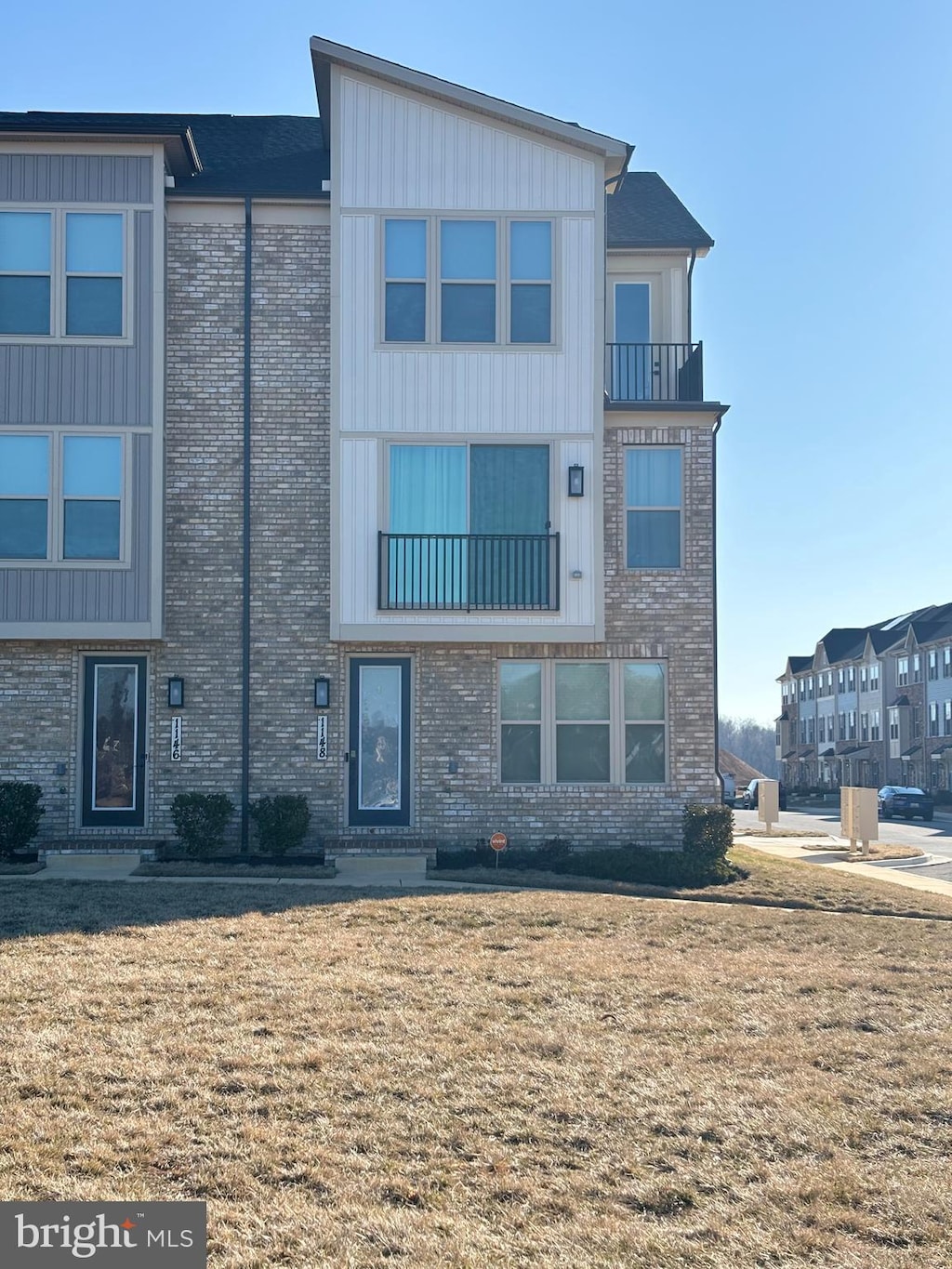 townhome / multi-family property featuring brick siding, a front lawn, and a balcony