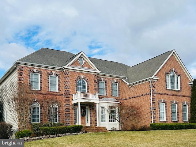 colonial home featuring a balcony, a front lawn, and brick siding