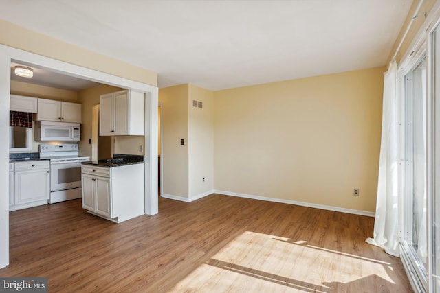 kitchen featuring dark countertops, white appliances, baseboards, and wood finished floors