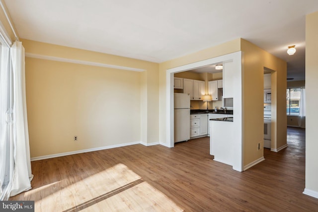 unfurnished living room featuring a sink, wood finished floors, and baseboards