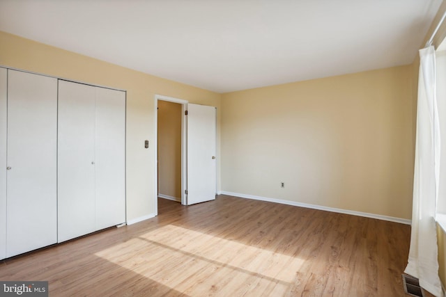 unfurnished bedroom with a closet, visible vents, baseboards, and wood finished floors