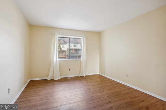 spare room with wood finished floors, visible vents, and baseboards