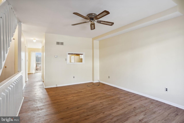 spare room with a ceiling fan, wood finished floors, visible vents, and baseboards