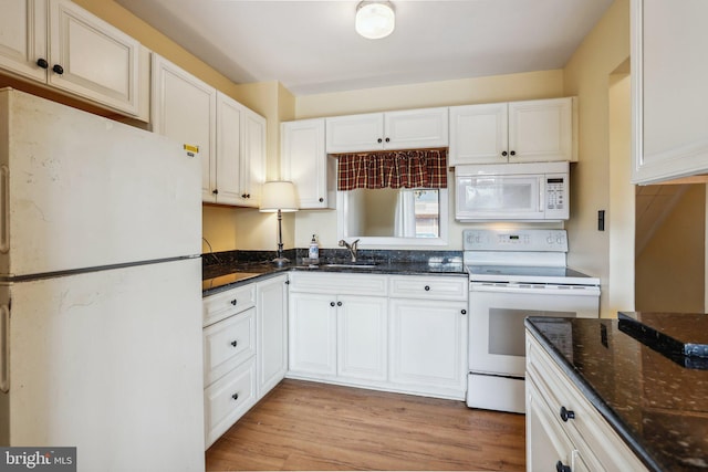 kitchen featuring light wood-style floors, white cabinets, a sink, dark stone counters, and white appliances