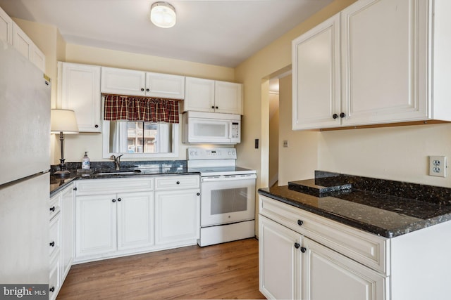 kitchen with white appliances, a sink, white cabinets, light wood finished floors, and dark stone countertops