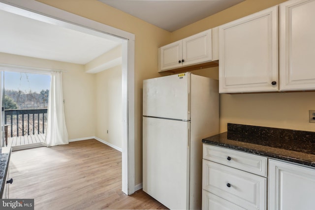 kitchen featuring white cabinets, dark stone countertops, freestanding refrigerator, and light wood-style floors