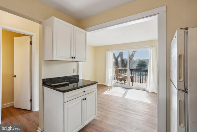 kitchen featuring white cabinetry, baseboards, light wood-style floors, freestanding refrigerator, and dark stone countertops