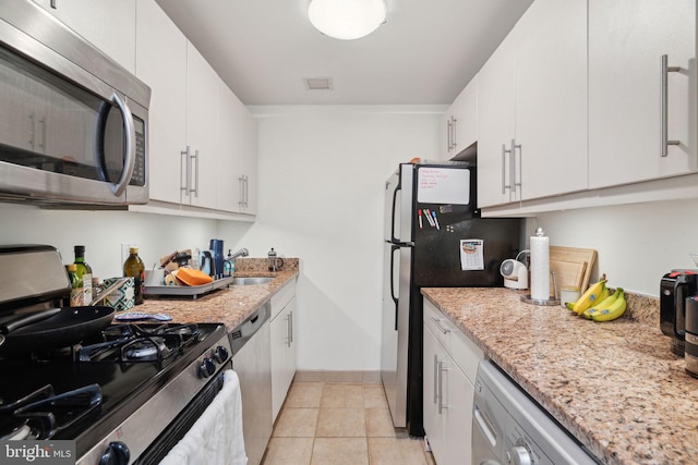 kitchen with light stone countertops, stainless steel appliances, light tile patterned flooring, white cabinetry, and a sink